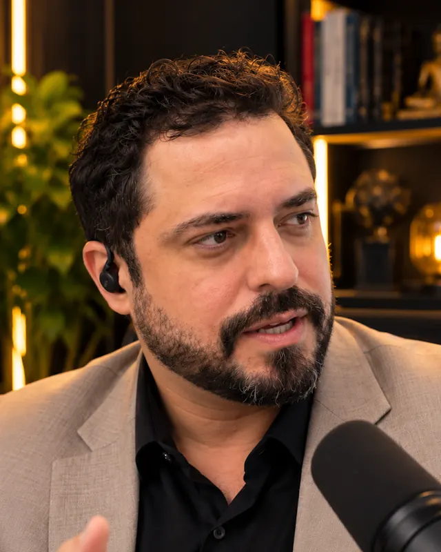 Dr. João Carlos Leitão conversando diante de um microfone, com estante de livros ao fundo